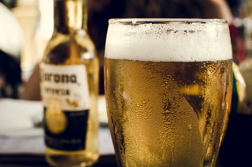 Close-up of chilled beer with frothy head next to a bottle on a bar table.